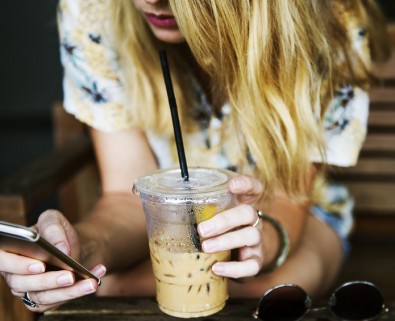 woman using phone drinking iced coffee